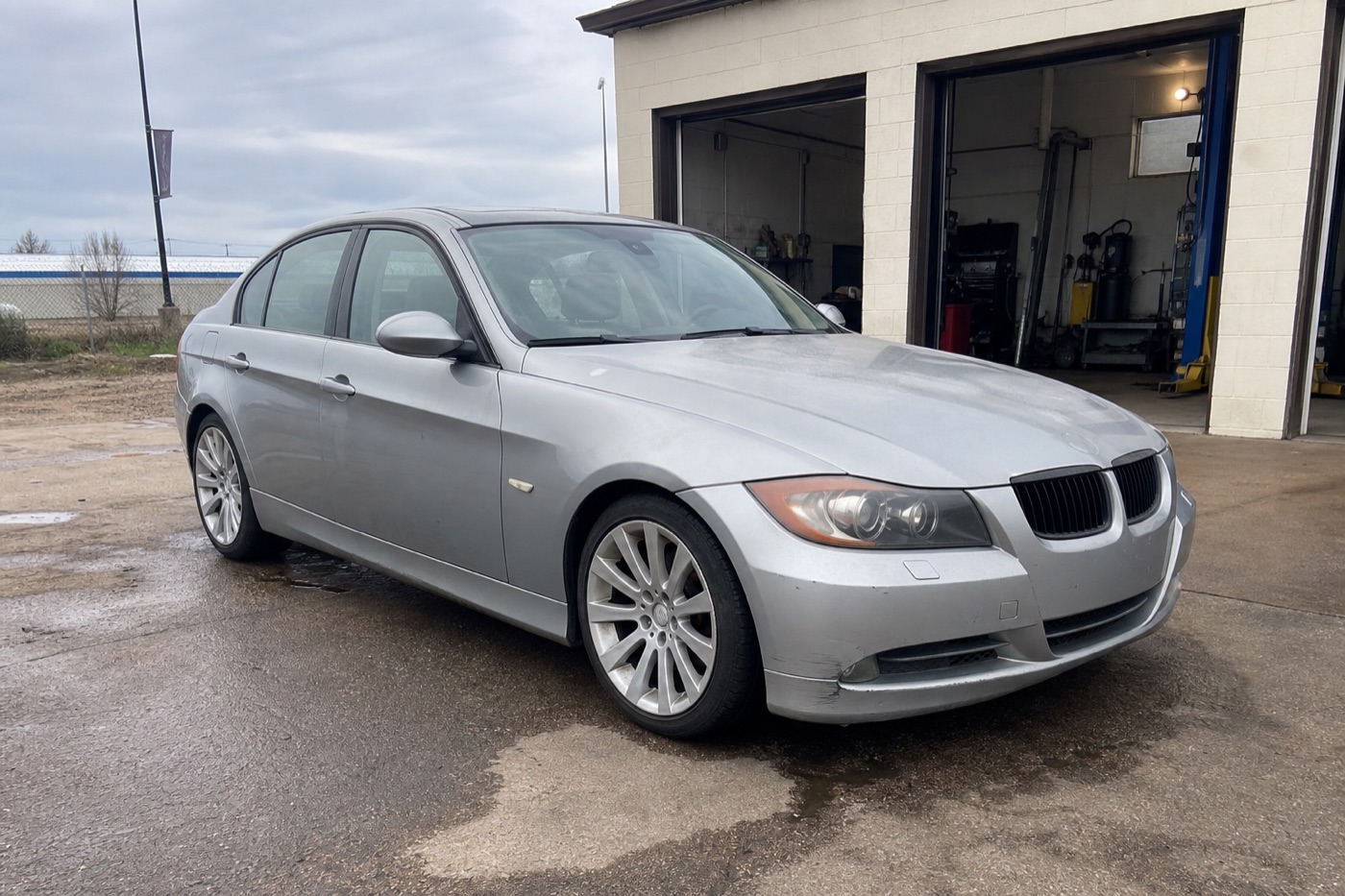 Worn silver 2006 BMW 330i project car outside an independent repair shop